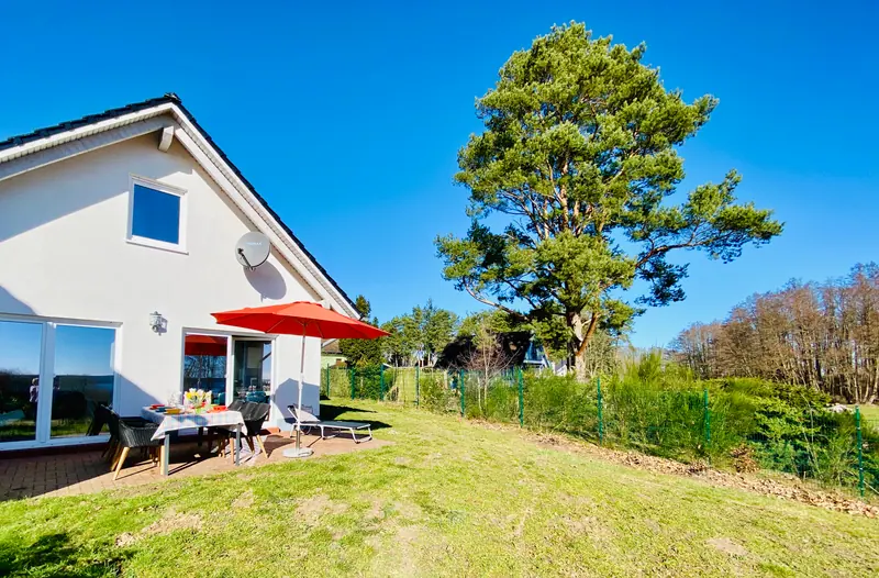 Außenansicht des Ferienhauses FriediSee mit Terrasse, Sonnenschirm und Kiefer
