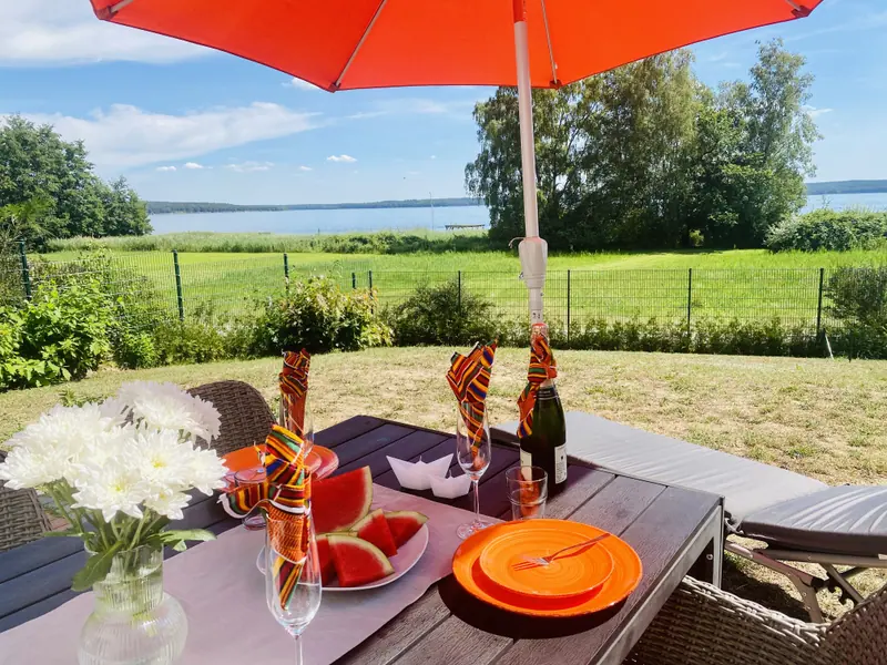 Terrassentisch mit Blumen und Sonnenschirm, im Hintergrund der Plauer See
